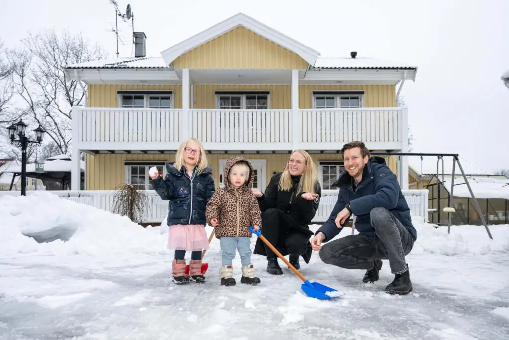Familjen Linde i Fagersta framför sitt gula och vita trähus. Lite snö på marken och barnen håller i varsin spade för att skotta.